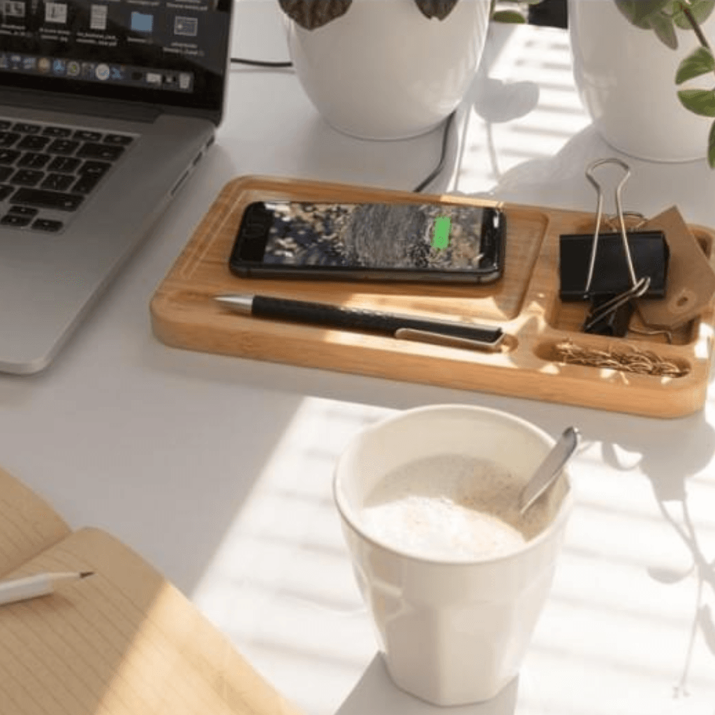 Bureau-opstelling met open laptop, bamboe organizer met smartphone, pen en klemmen, een notitieboek en een witte mok warme drank in zonlicht.